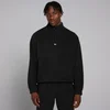 Een man draagt een zwarte fleecevest met een kwartrits en een klein wit logo.