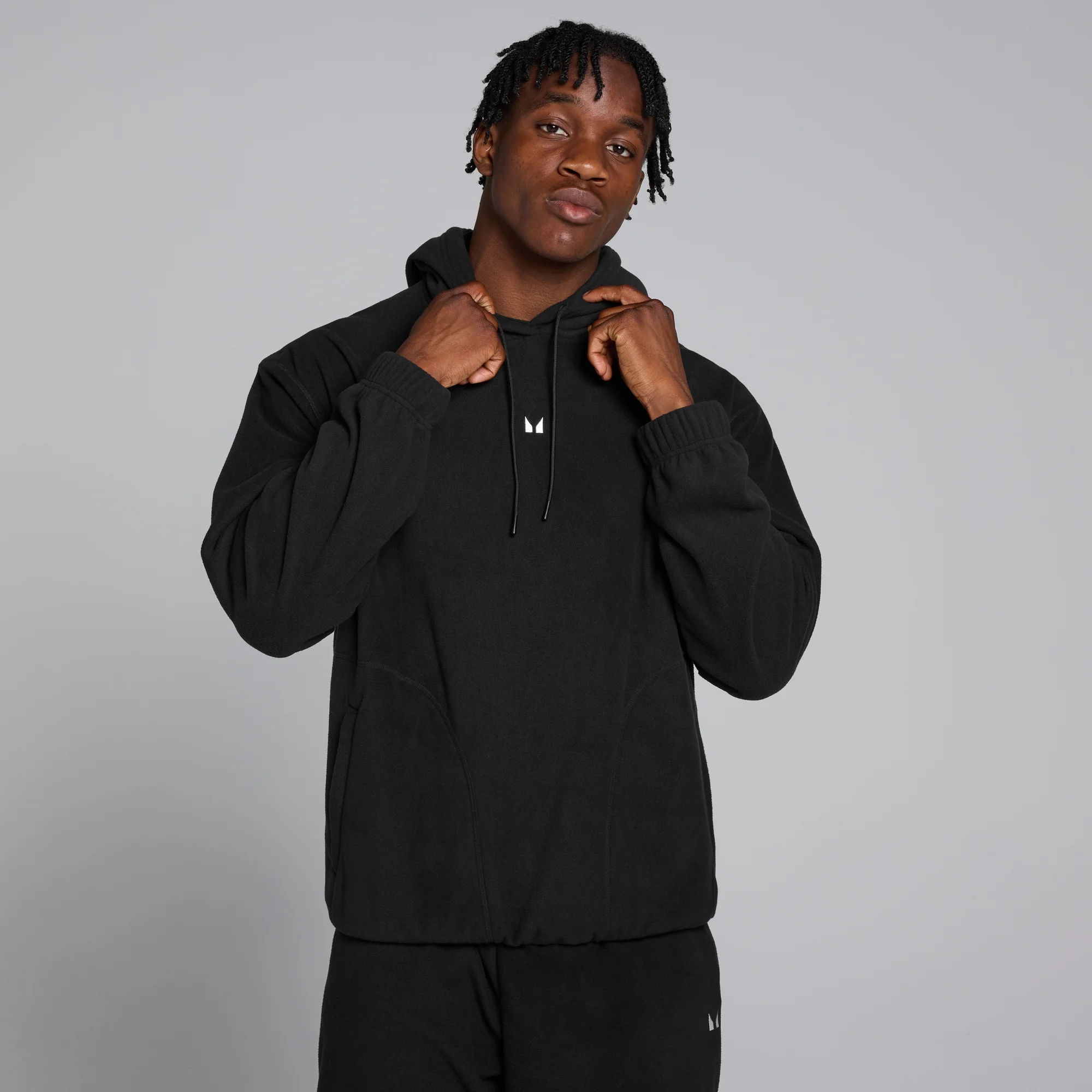 Een man draagt een zwarte fleece hoodie met een wit MP logo op de borst.