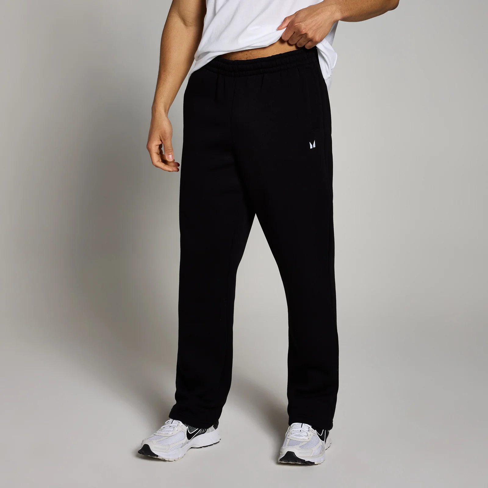 Een man draagt een zwarte joggingbroek met rechte pijpen en een klein wit logo.
