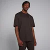 Een man draagt een koffiebruin, oversized T-shirt met korte mouwen en een klein wit logo.