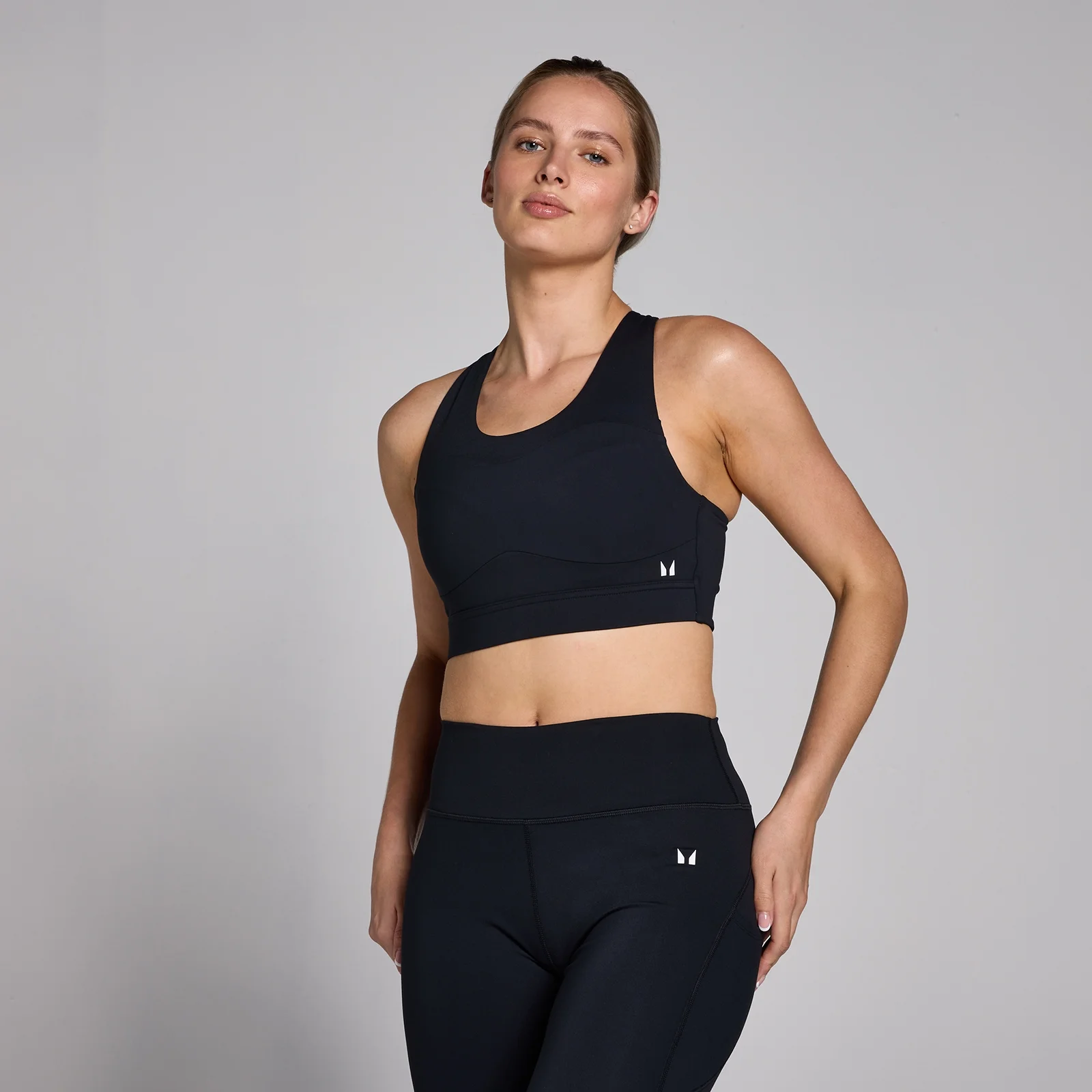 Een vrouw draagt een zwarte sportbeha en legging met een klein wit logo.