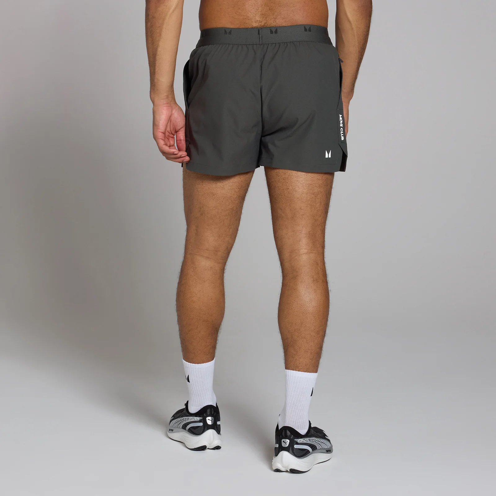 Een man draagt een korte, donkergrijze sportbroek met witte sokken en sportschoenen.