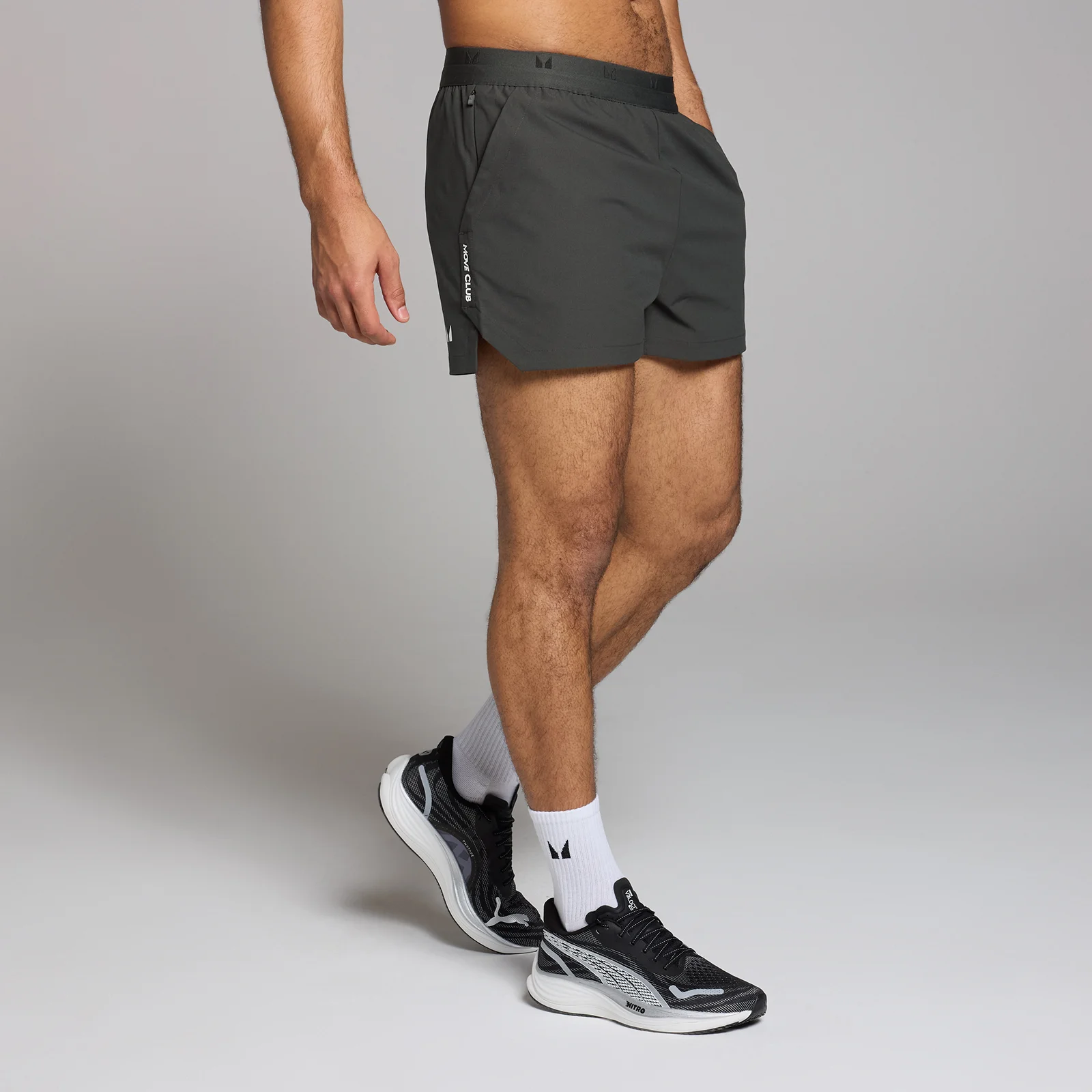 Een man draagt zwarte, korte sportbroeken met een klein logo, witte sokken en zwarte sportschoenen.