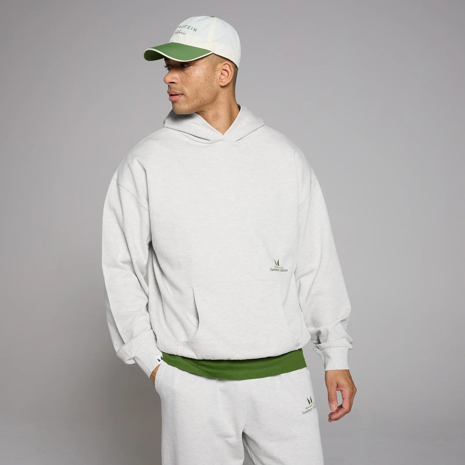 Een man draagt een gemêleerde grijze oversized hoodie met capuchon en een klein logo.