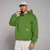 Een man draagt een donkerdennengroene oversized hoodie met capuchon en een zak aan de voorkant.