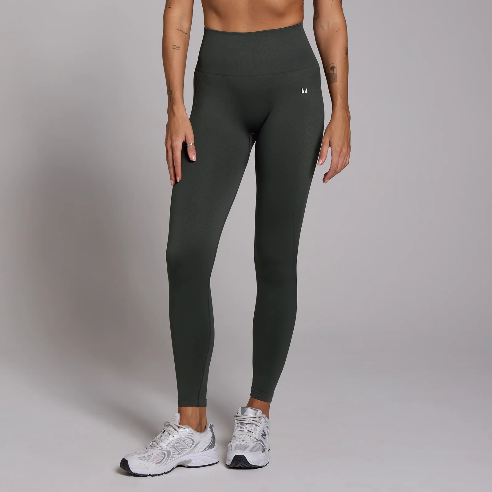 Een vrouw draagt een donkergroene, naadloze 7/8 legging met een hoge taille en witte sneakers.