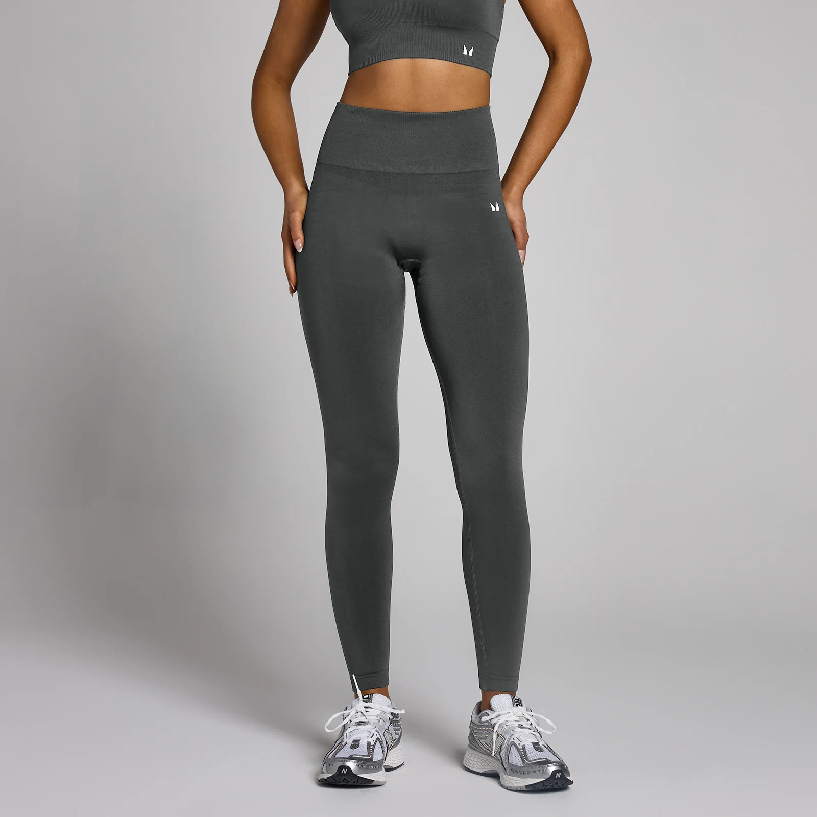 Een vrouw draagt een nachtgrijze, naadloze legging met hoge taille en een klein logo.