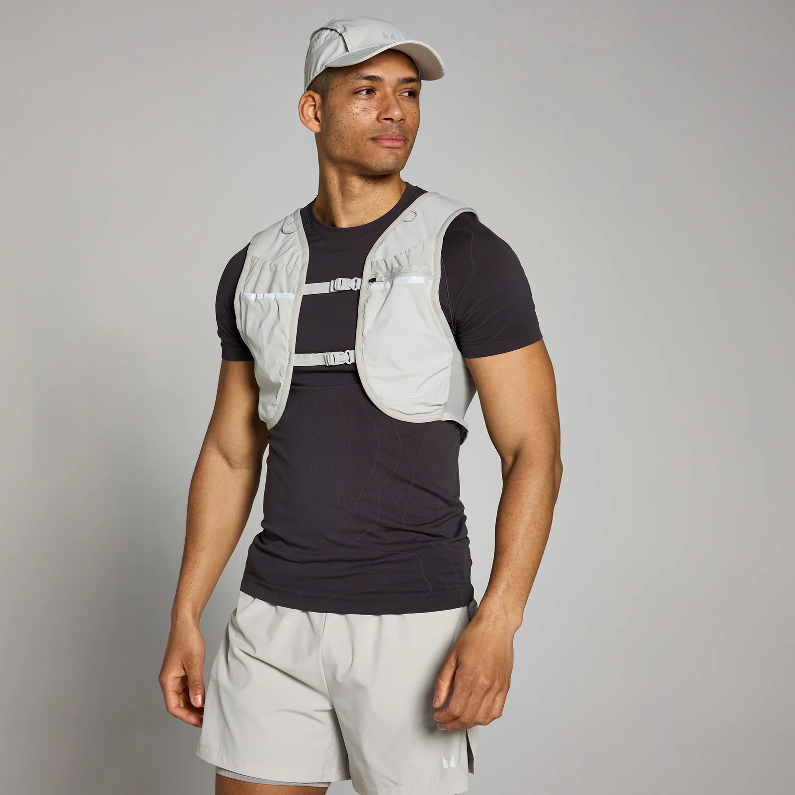 Een man draagt een grijs hydratatievest over een zwart shirt, met een bijpassende pet en korte broek.
