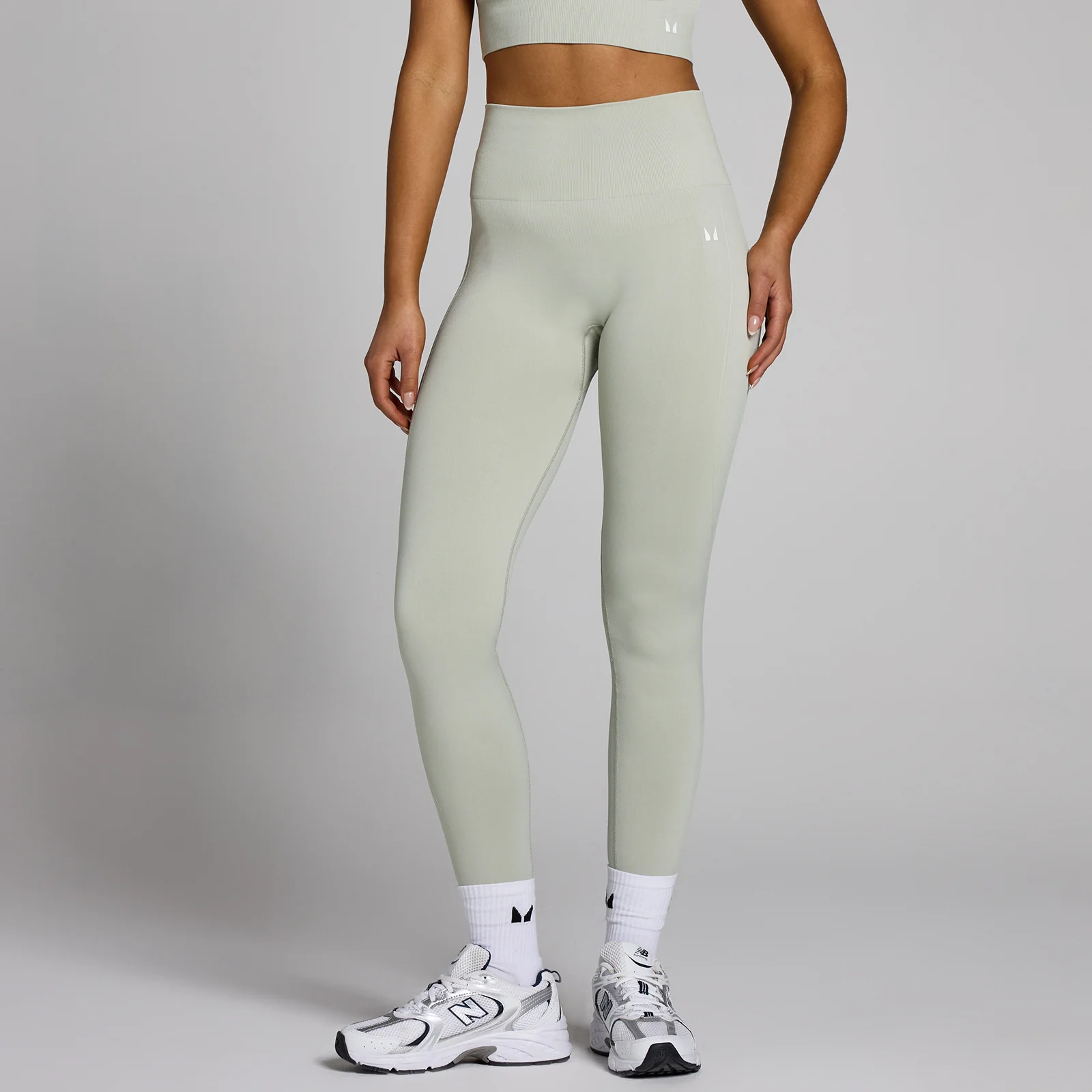 Een vrouw draagt een lichtgroene, naadloze legging met hoge taille en witte sportschoenen.