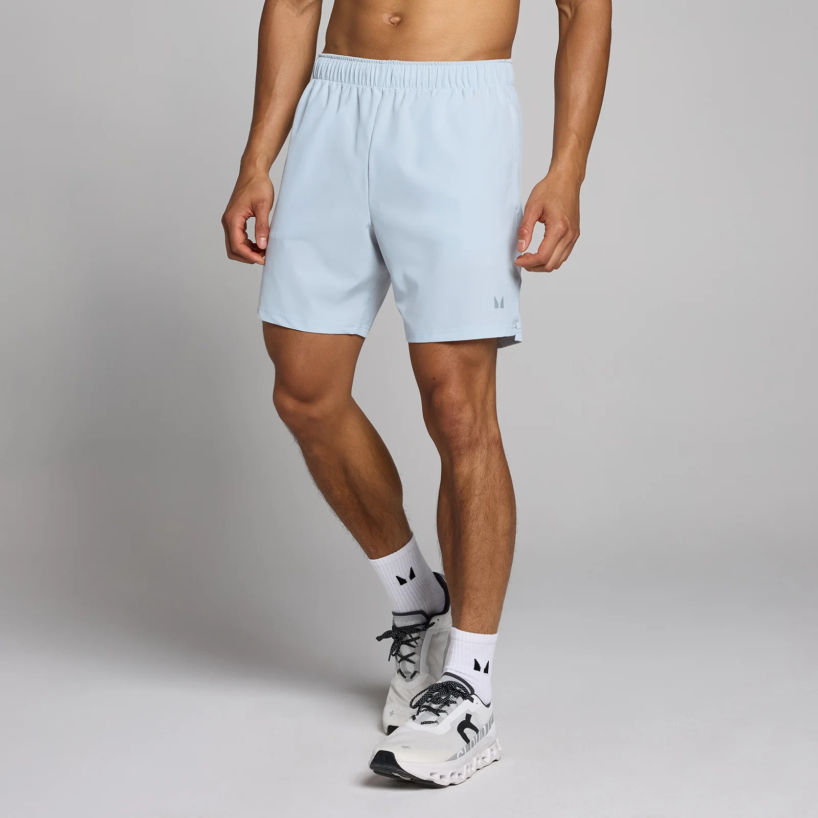 Een man draagt een ijsgrijze MP Tempo short met een elastische tailleband en witte sportschoenen.