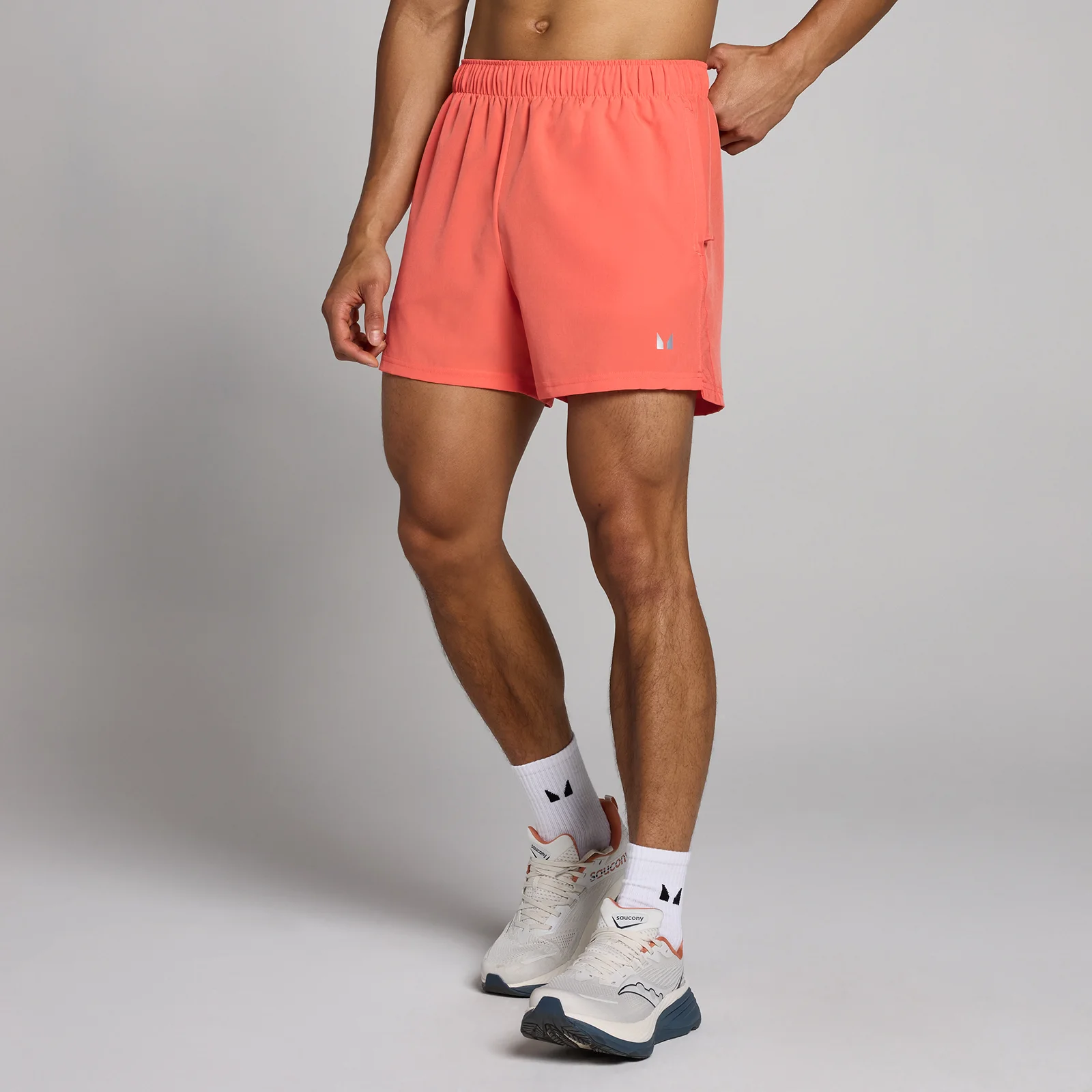 Een man draagt een korte, koraalkleurige sportbroek met een elastische tailleband en een klein logo.