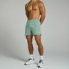 Een man draagt een vaalgroene, korte sportbroek met een elastische tailleband en een klein wit logo.