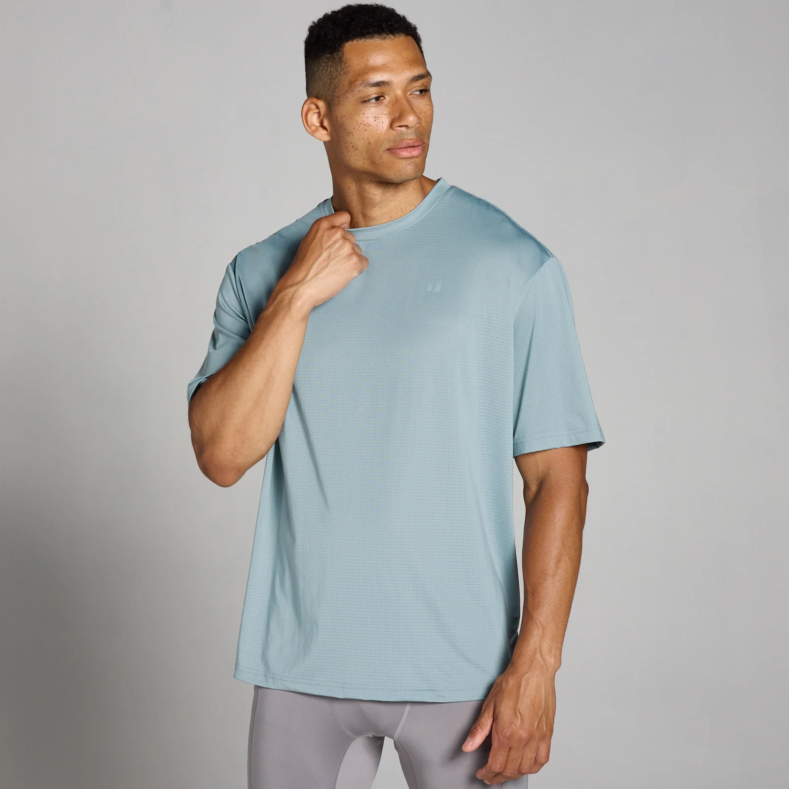 Een man draagt een loodgrijs, oversized trainingsshirt van mesh met korte mouwen.