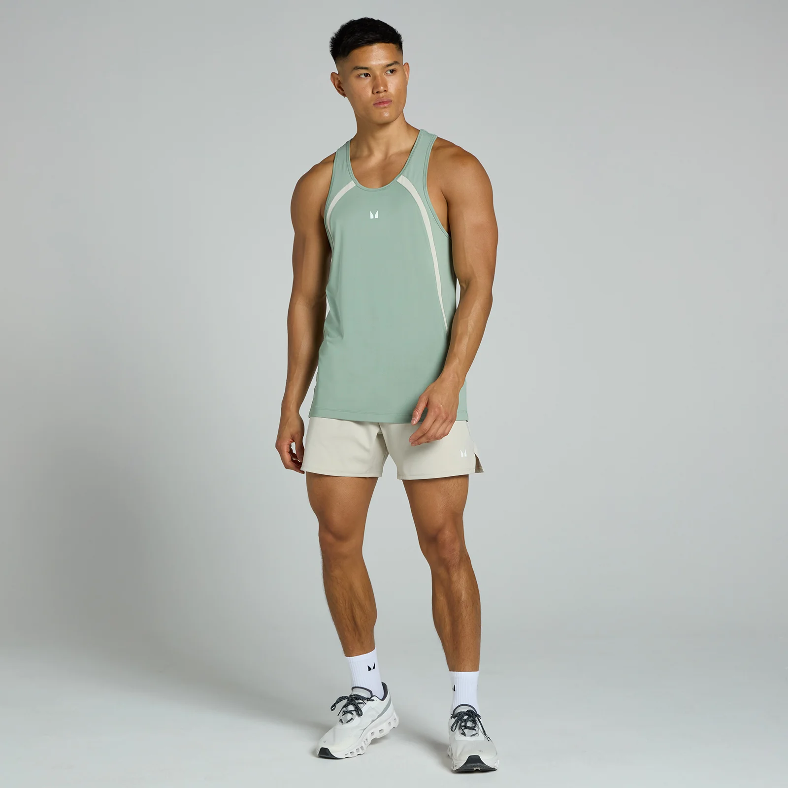 Een man draagt een vaalgroen hemd met witte accenten en beige shorts, staand tegen een grijze achtergrond.