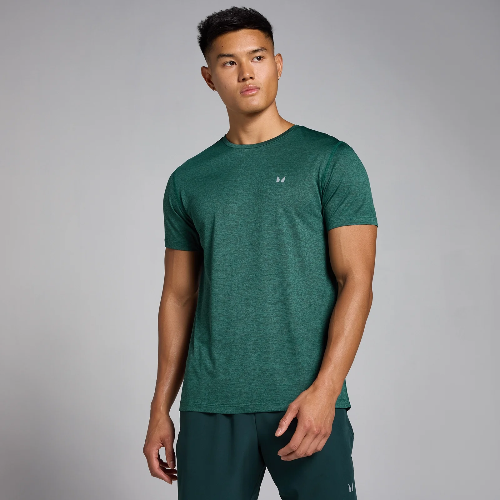 Een man draagt een donkergroen gemêleerd T-shirt met korte mouwen en een klein logo.