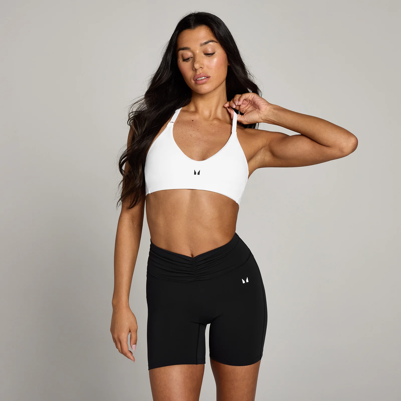 Een vrouw draagt een witte sportbeha met halternek en een zwarte sportshort.