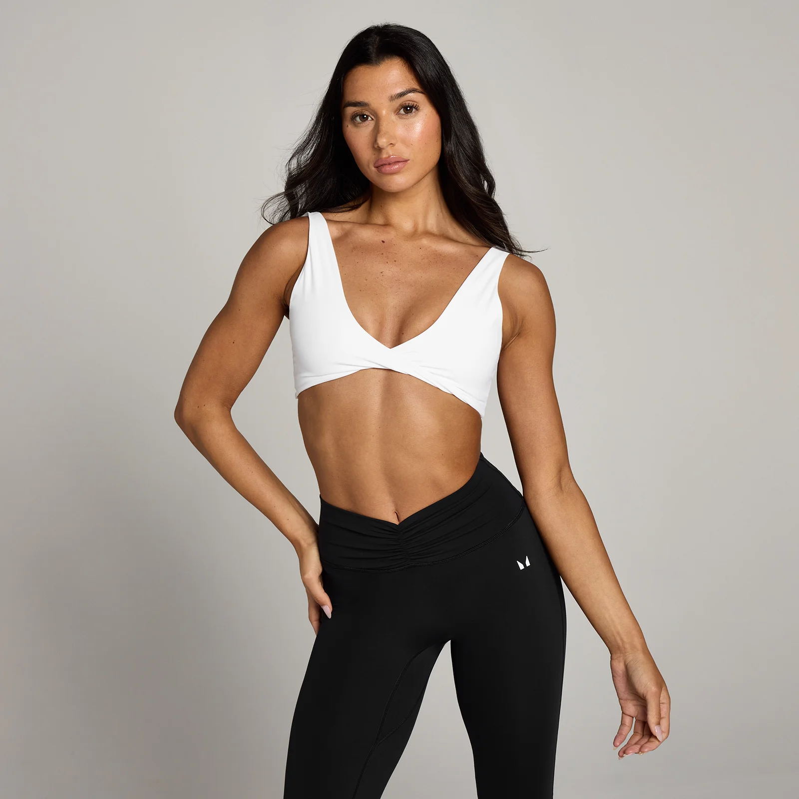 Een vrouw draagt een witte sportbeha met gedraaide voorkant en een zwarte legging.