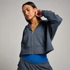 Een vrouw draagt een donkergrijze, korte hoodie met rits en een blauwe top.