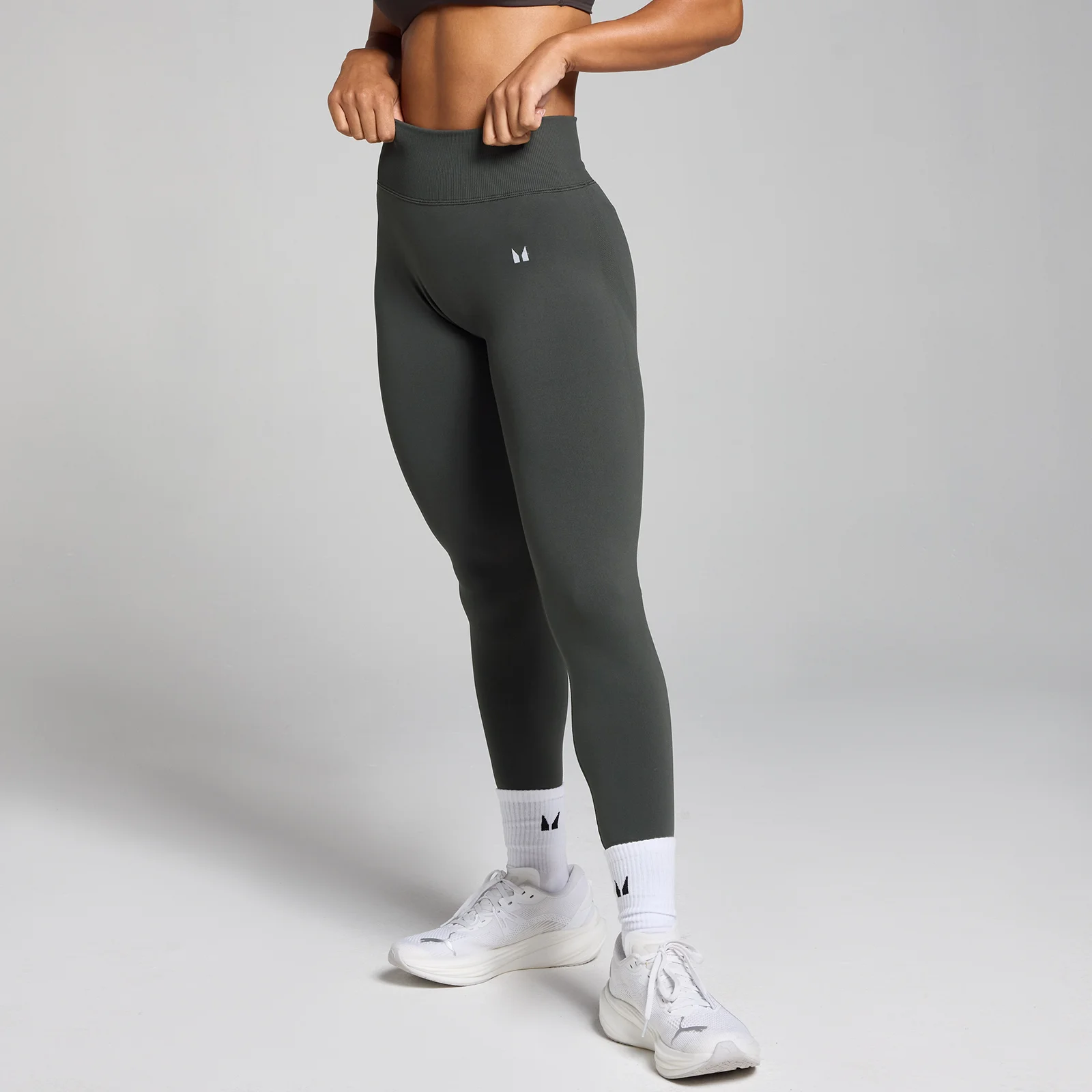 Een vrouw draagt een nachtgrijze, middelhoge, naadloze legging met een klein logo op de heup.