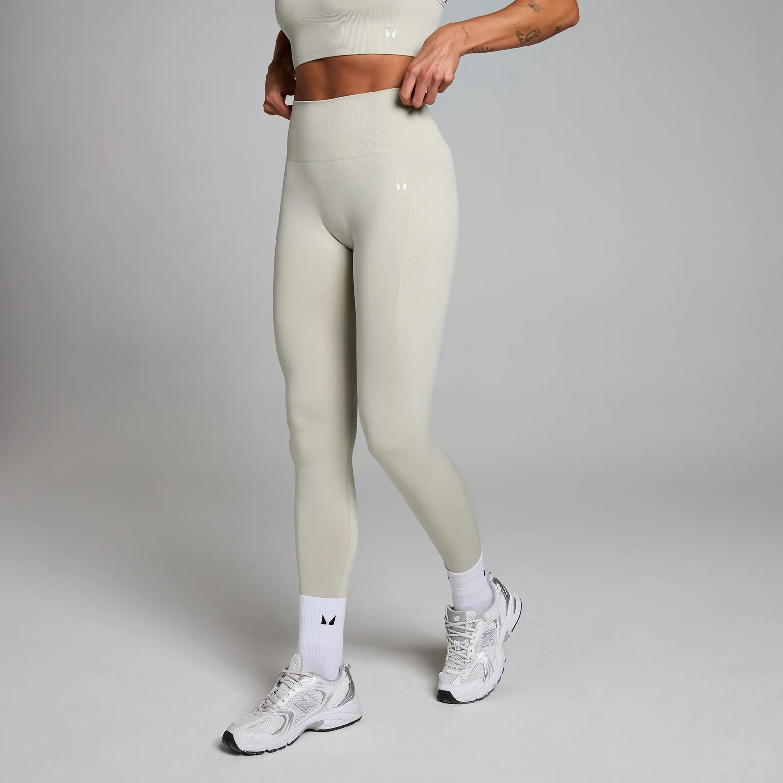 Een asgrijze, naadloze legging met hoge taille, gedragen door een persoon met witte sokken en sportschoenen.