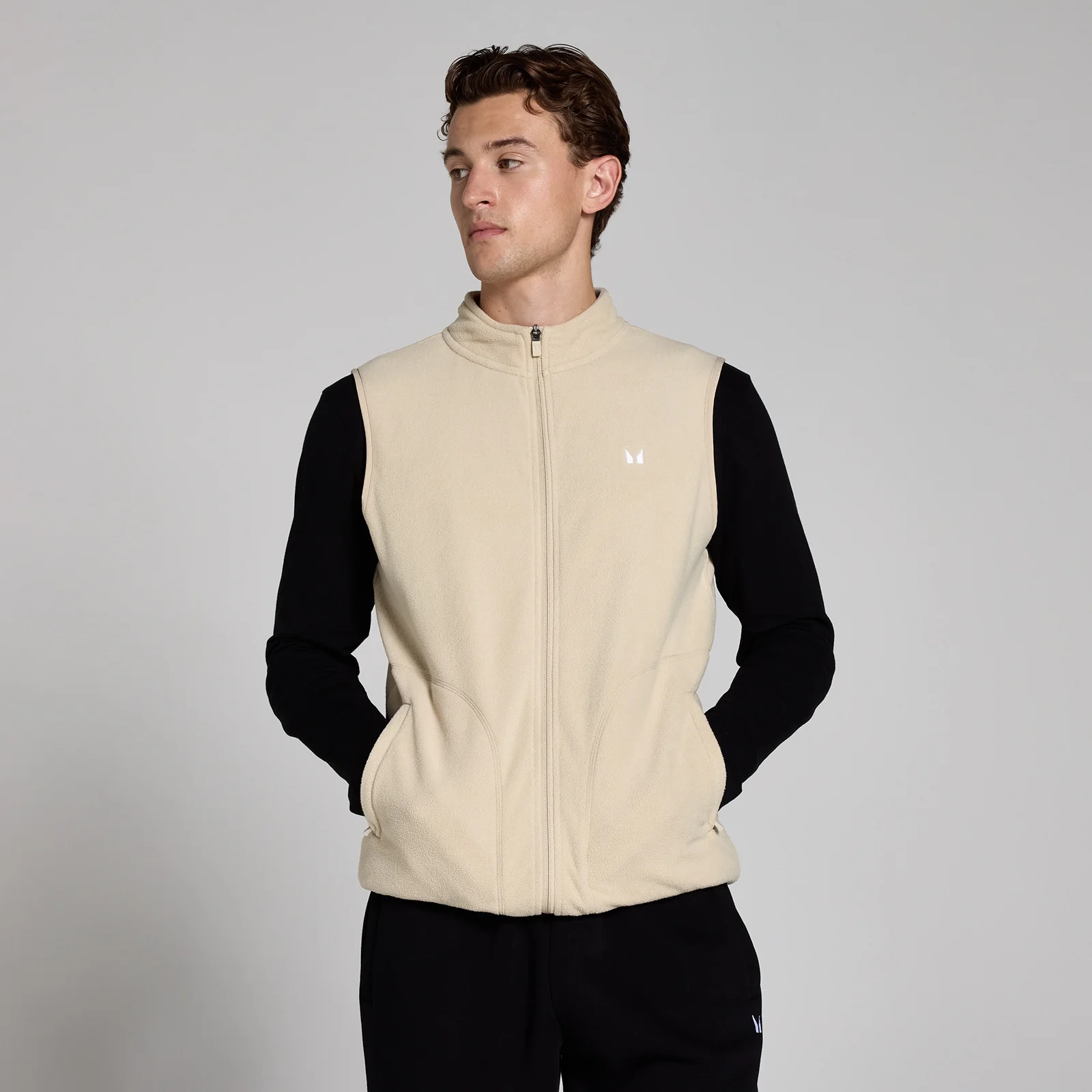 Een man draagt een haverwitte fleece gilet met rits en een klein wit logo.
