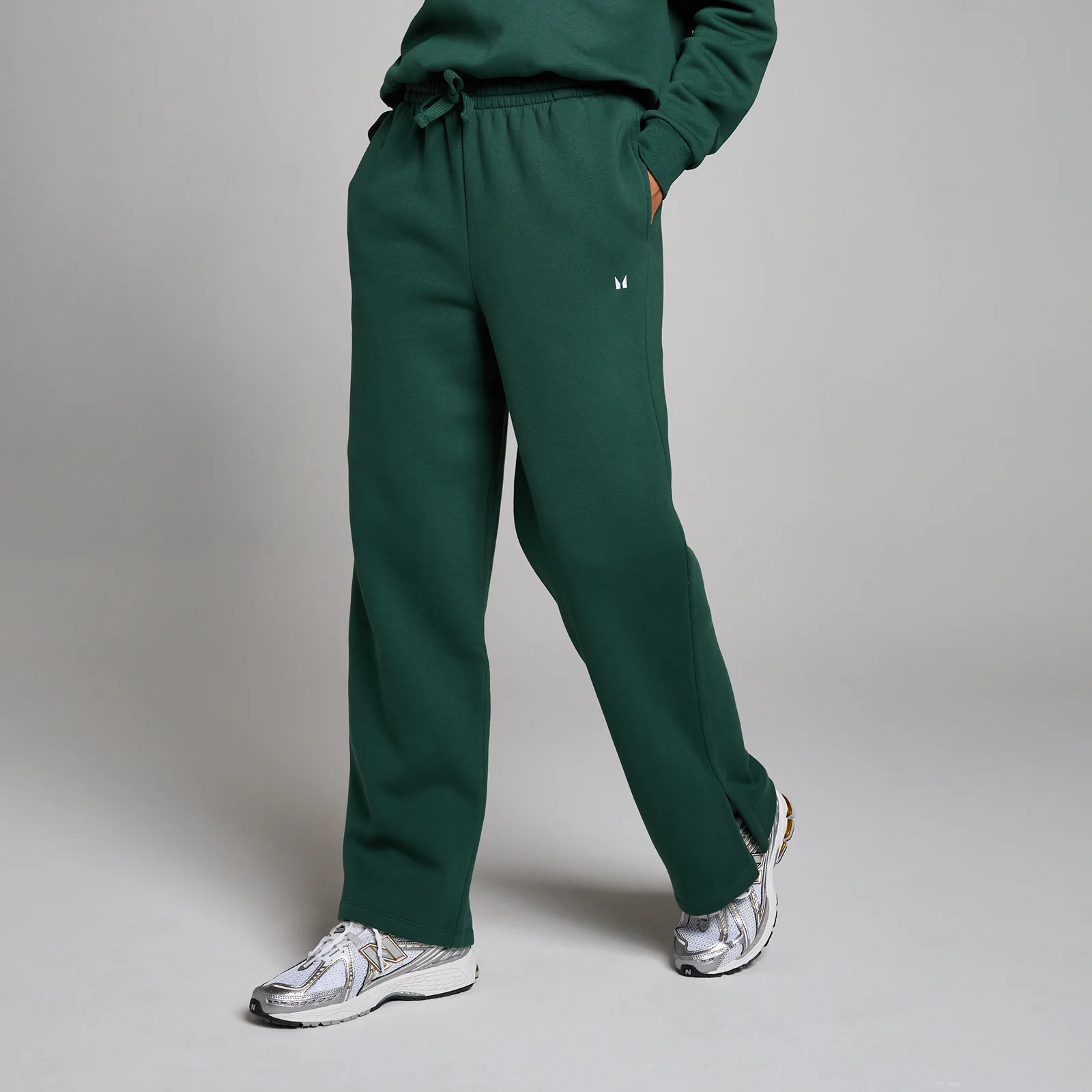 Een persoon draagt een racegroene joggingbroek met rechte pijpen en een klein wit logo.