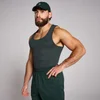 Een man draagt een mouwloze, geribbelde, donkergrijze tanktop en een groene pet en broek.