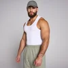 Een man draagt een witte, geribbelde tanktop en een groene pet en joggingbroek.