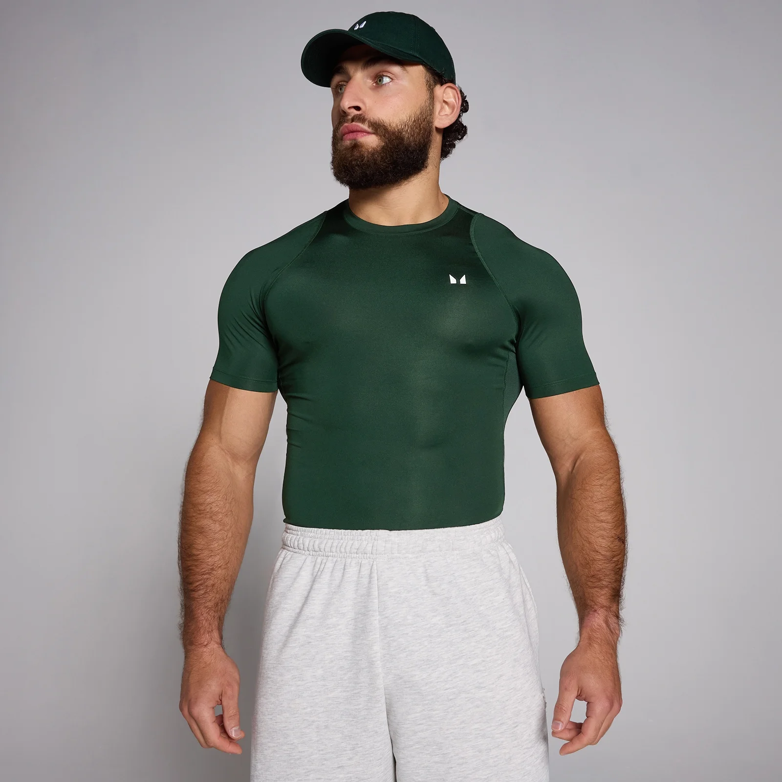 Een man draagt een donker smaragdgroen trainingsshirt met korte mouwen en een bijpassende pet.