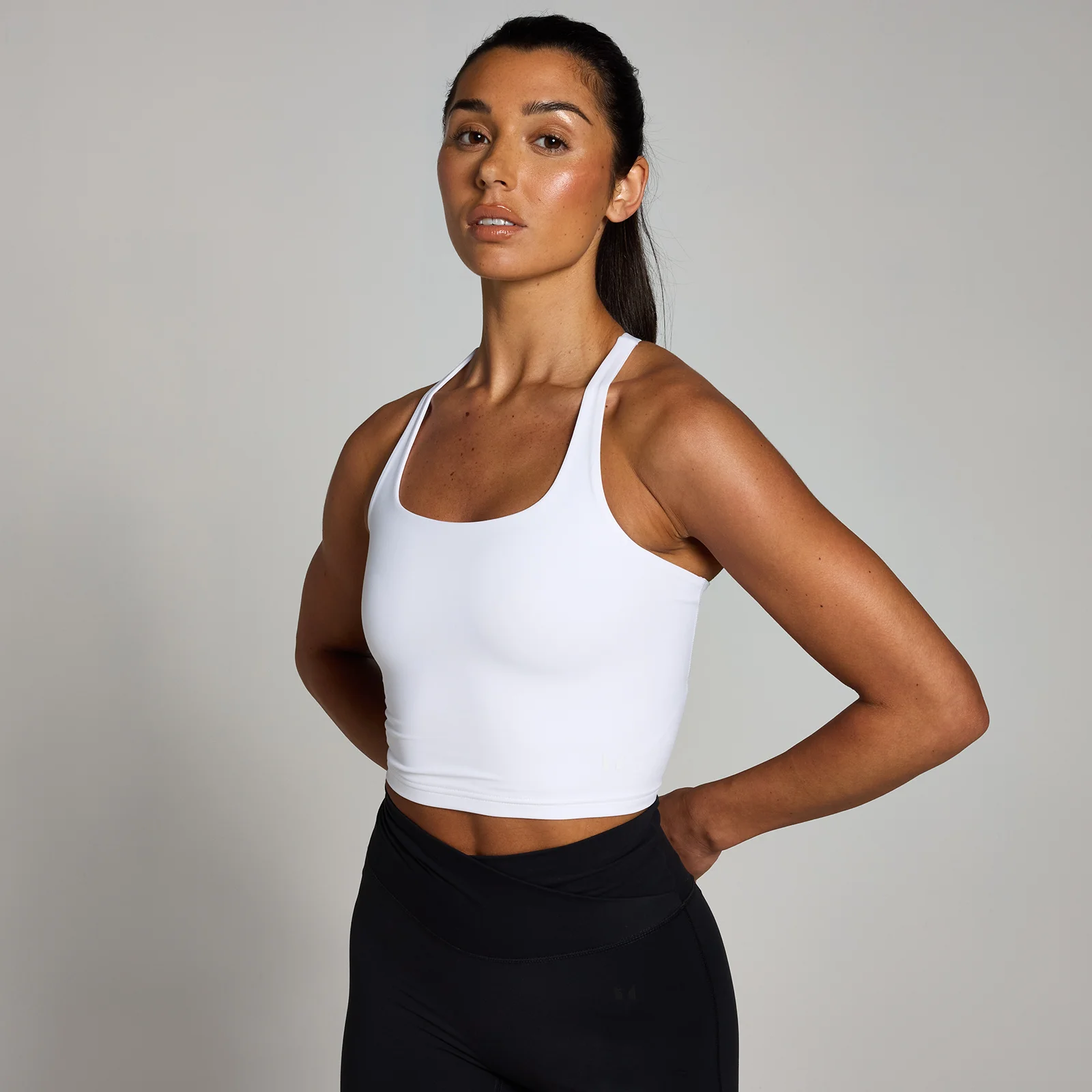 Een witte, mouwloze sporttop met racerback, gedragen door een vrouw met zwarte legging.