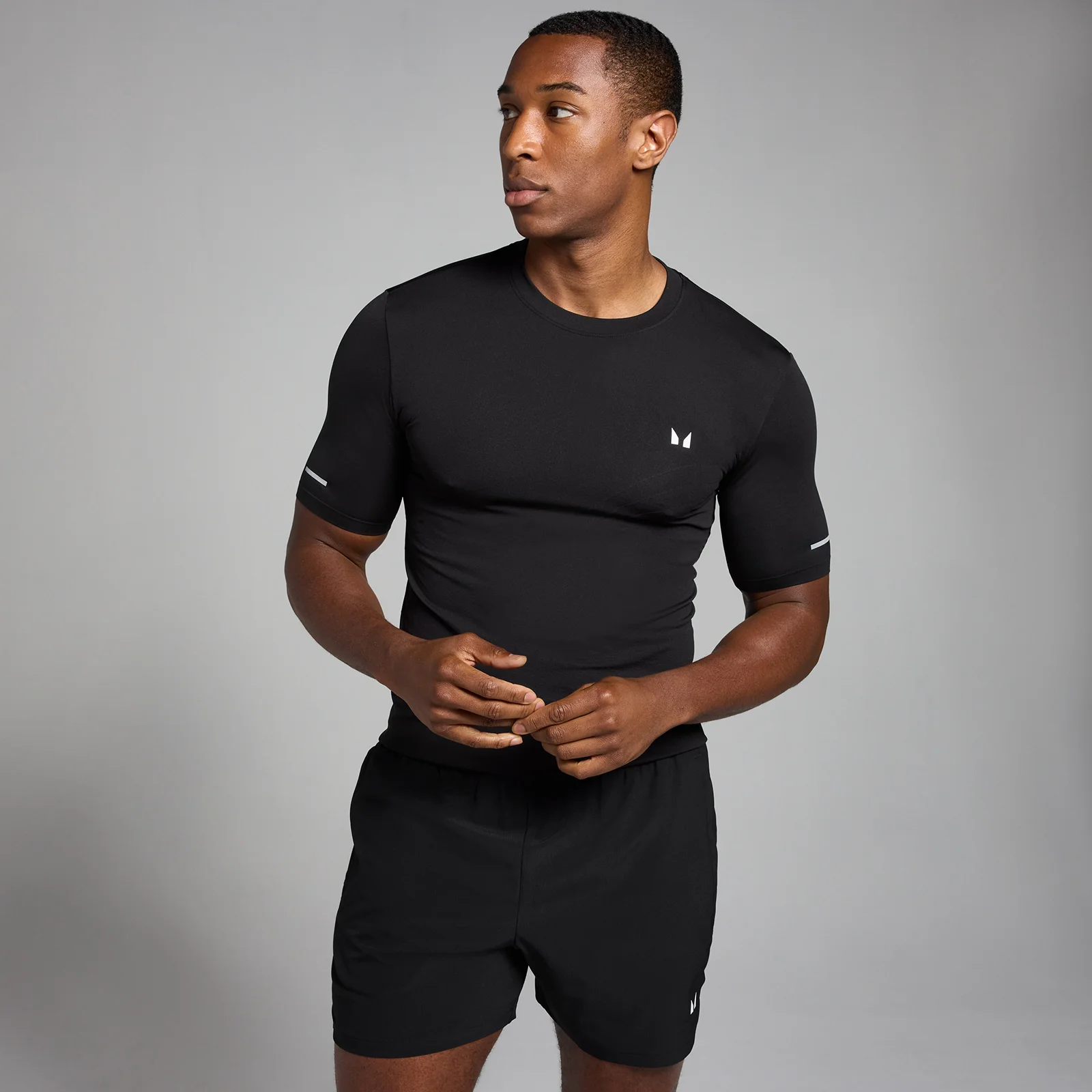 Een man draagt een zwart, nauwsluitend T-shirt met korte mouwen en een klein wit logo.