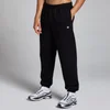 Een zwarte, oversized joggingbroek met elastische tailleband en een klein wit logo op het been.