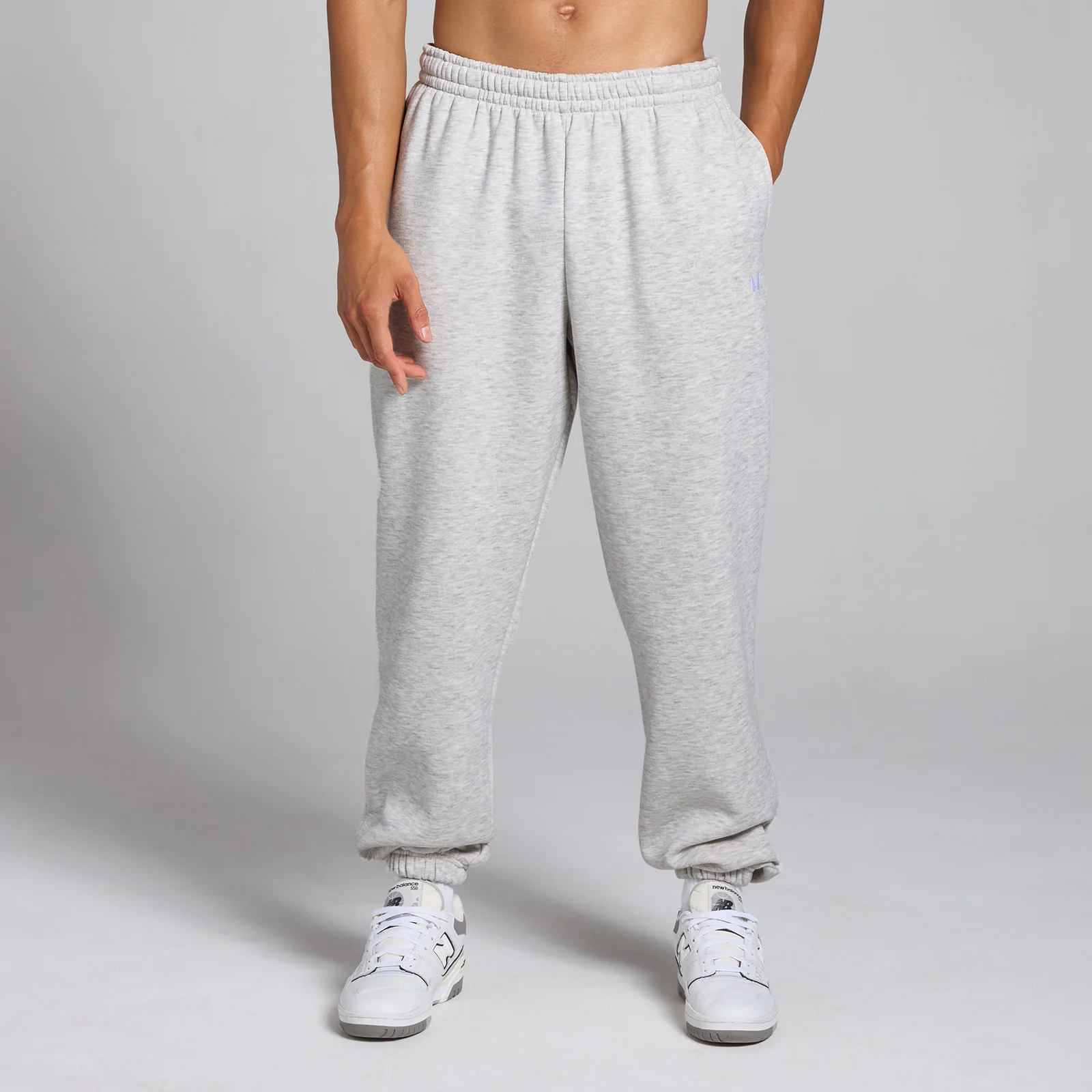 Een persoon draagt een gemêleerde lichtgrijze joggingbroek met elastische tailleband en enkels.