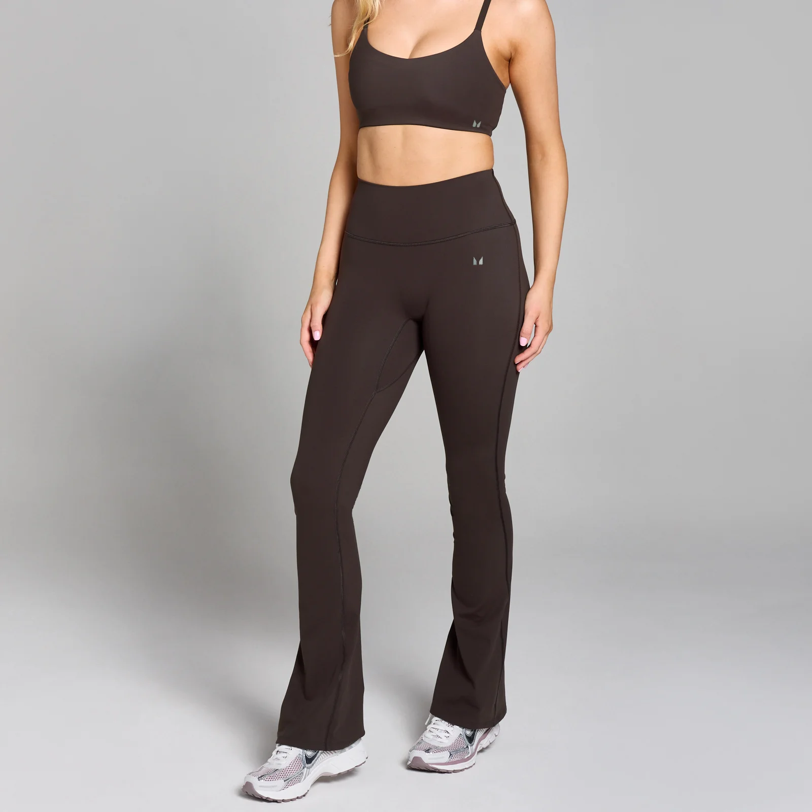 Een vrouw draagt een cacaobruine sportbeha en uitlopende legging met hoge taille.