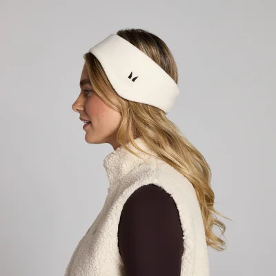 Een lichtroomwitte fleece oorwarmer met een klein zwart logo, gedragen door een vrouw.