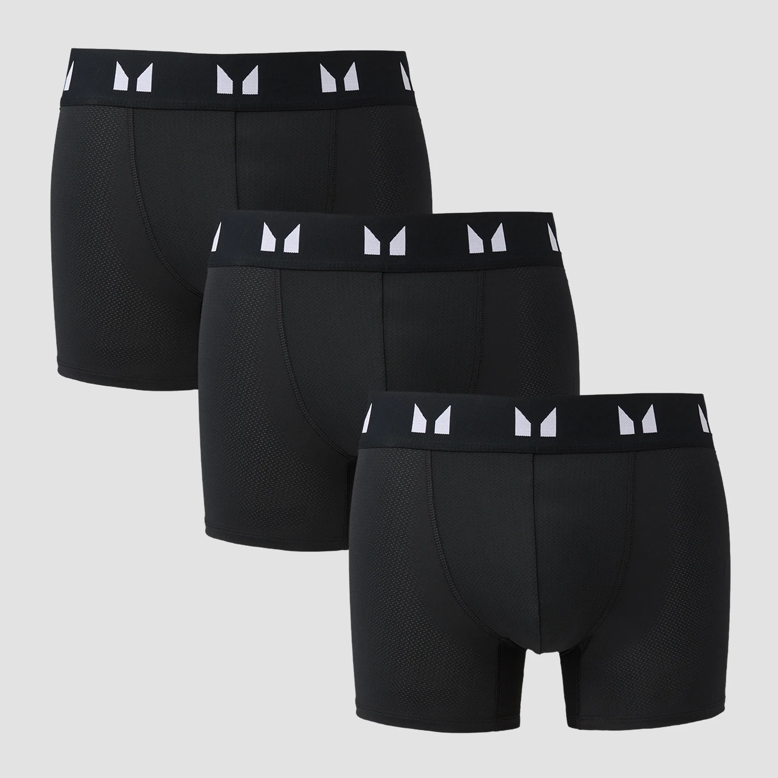 Drie zwarte boxershorts met een witte band met logo, gestapeld op een grijze achtergrond.