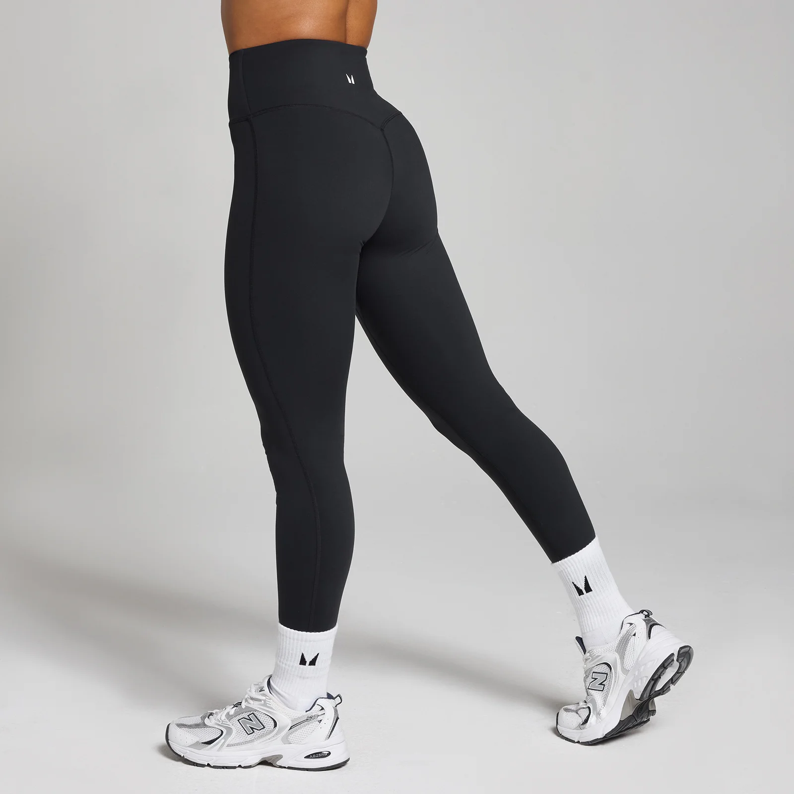 Een vrouw draagt een zwarte, hoge taille legging met witte sokken en sportschoenen.