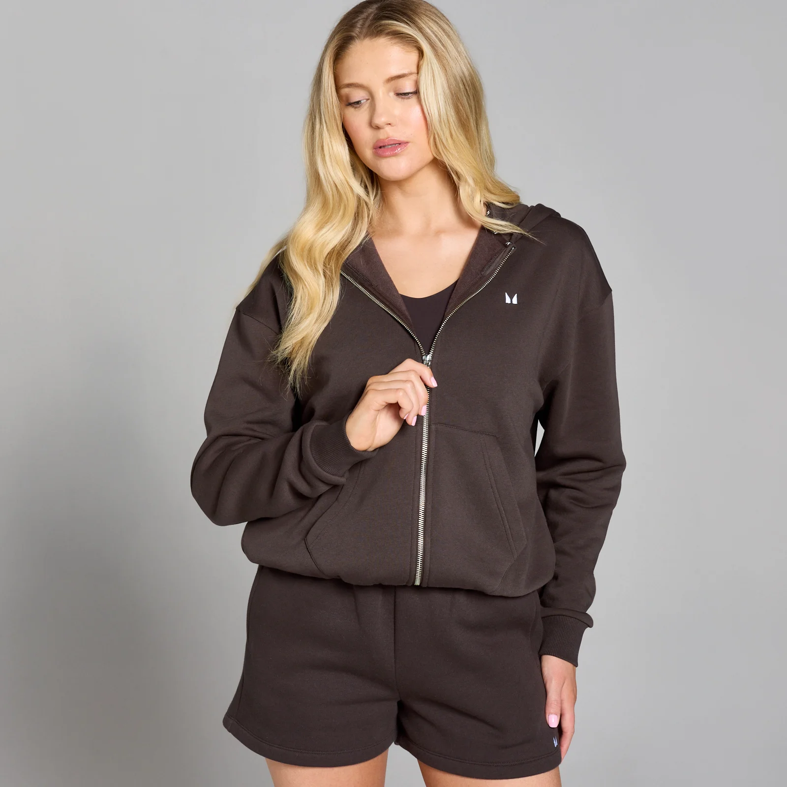 Een vrouw draagt een chocoladebruine hoodie met rits en bijpassende shorts.