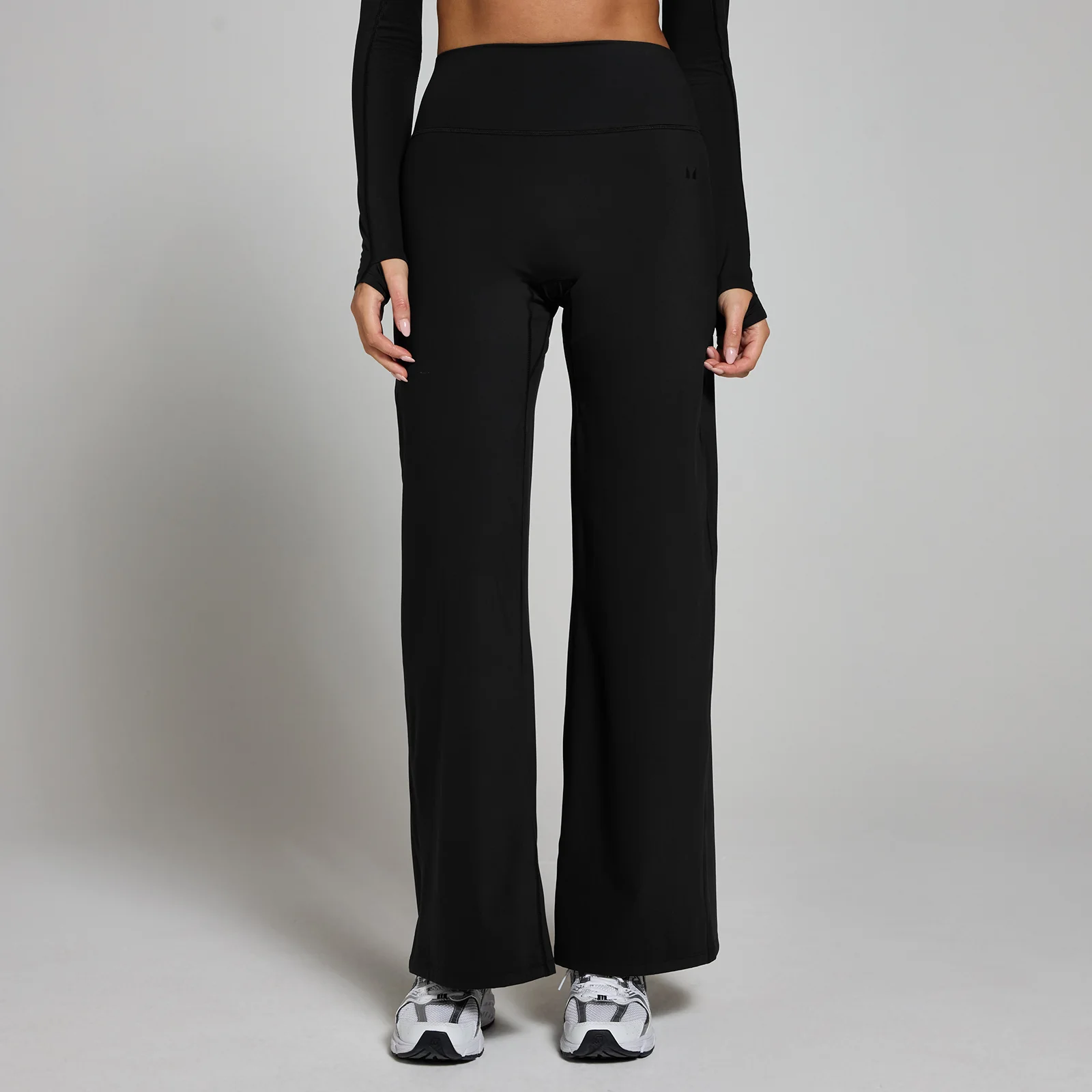 Een vrouw draagt een zwarte legging met wijde pijpen en witte sportschoenen.