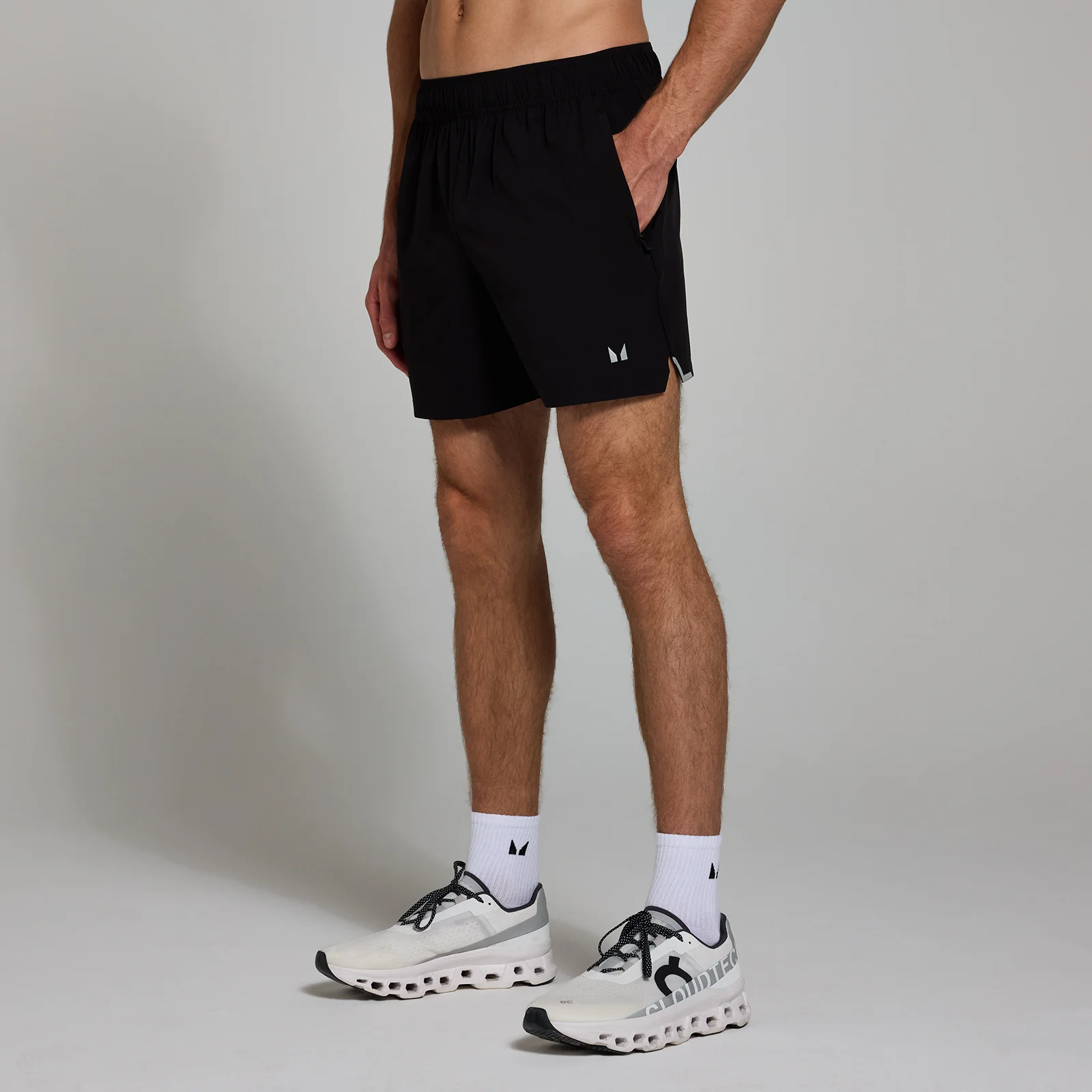 Een man draagt een zwarte, geweven sportshort met een klein, wit logo op de pijp.