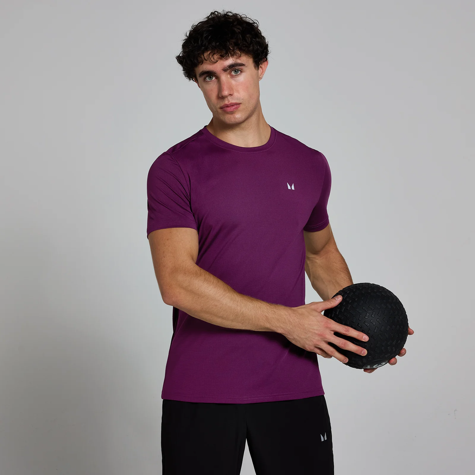 Een man draagt een pruimenpaars T-shirt met korte mouwen en een klein wit logo.