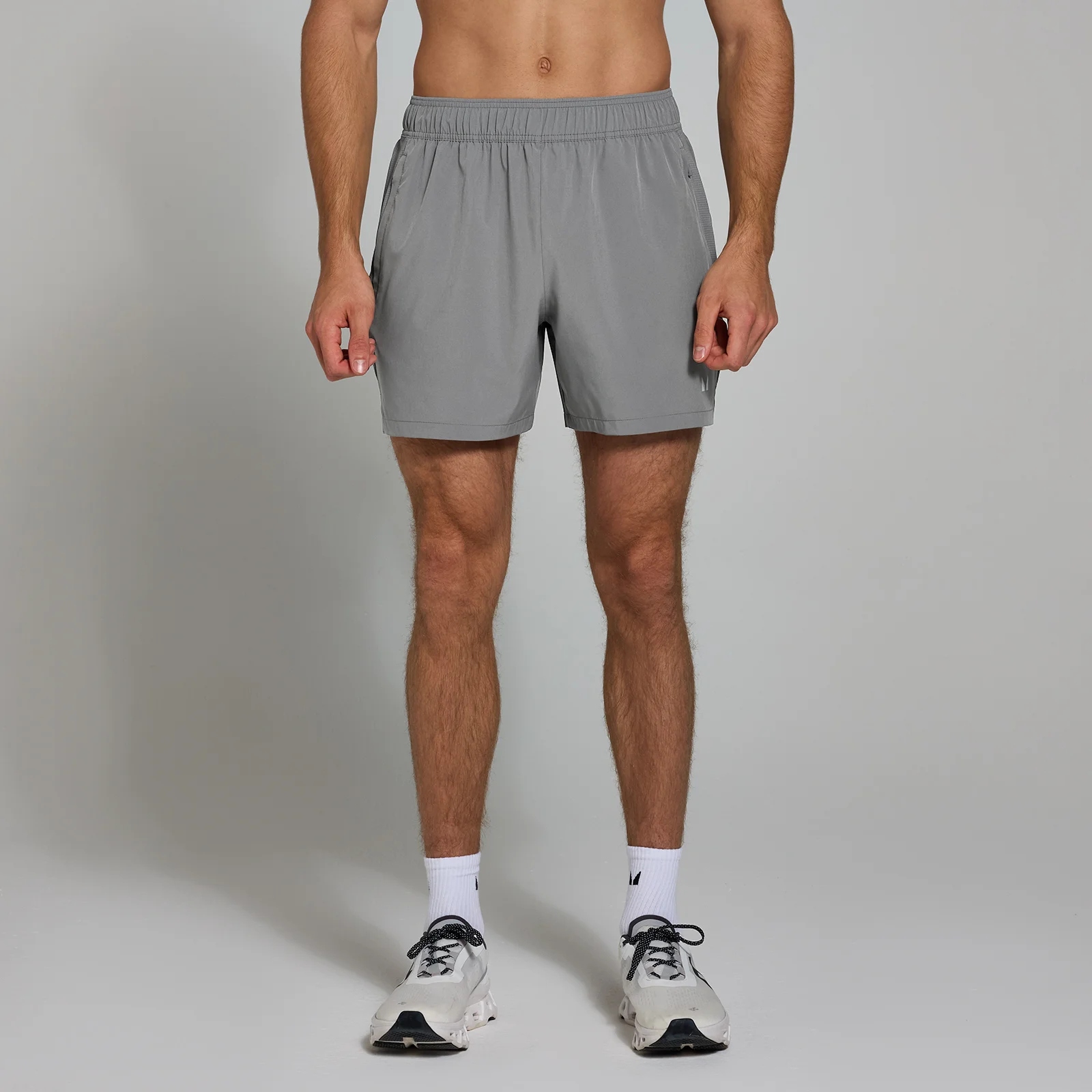 Een man draagt een grijze, geweven sportshort met een elastische tailleband en zakken.