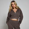 Een vrouw draagt een chocoladebruine hoodie met rits en bijpassende joggingbroek.