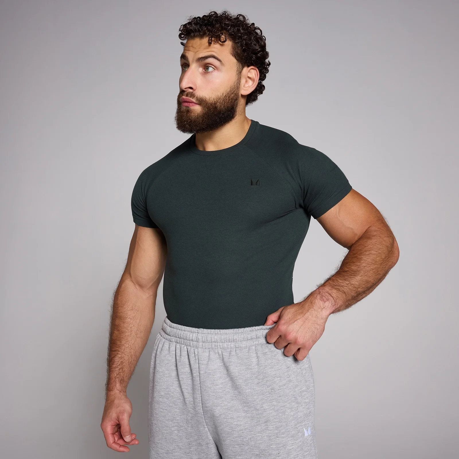 Een man draagt een donkergrijs, geribbeld T-shirt met korte mouwen en een klein logo.